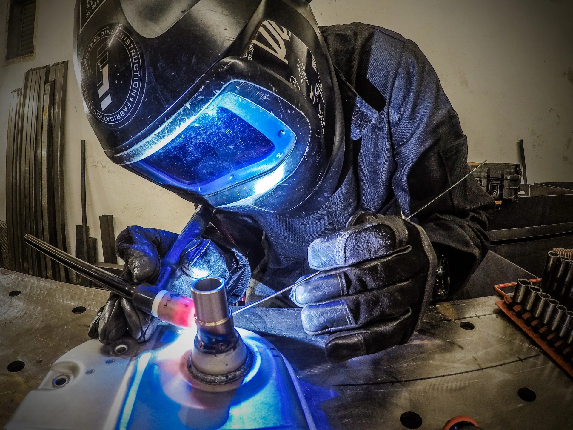 Lasser met helm voert TIG-laswerk uit aan een werkbank