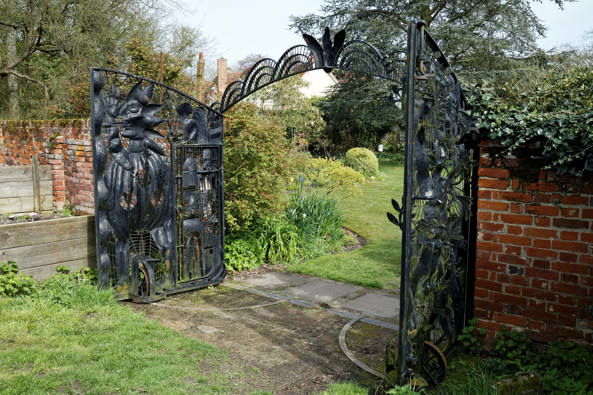 Open zwarte metalen tuinpoort met gesmede bladmotieven
