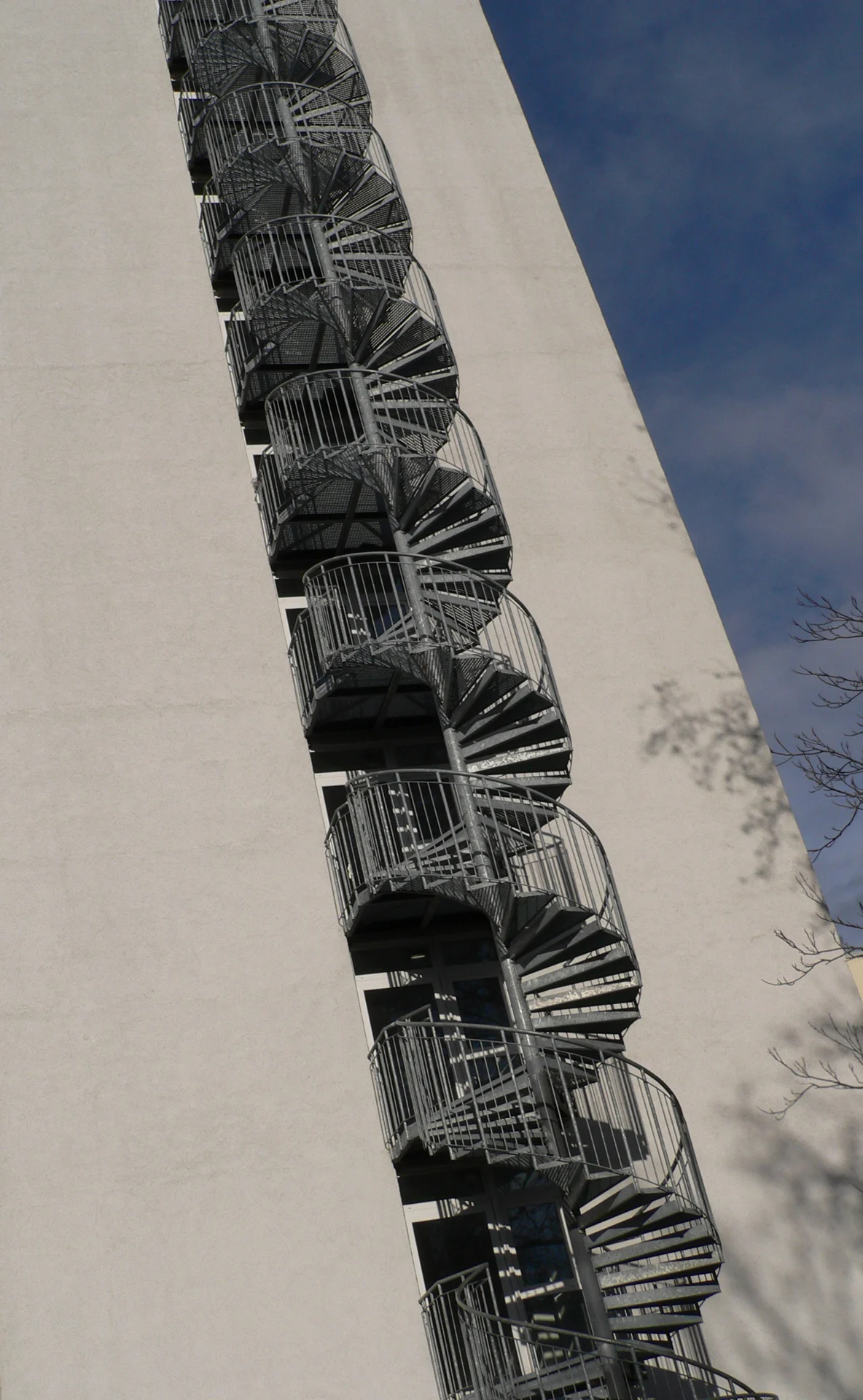 Hoge stalen spiltrap met roostertreden en verticale balusters aan een gebouw