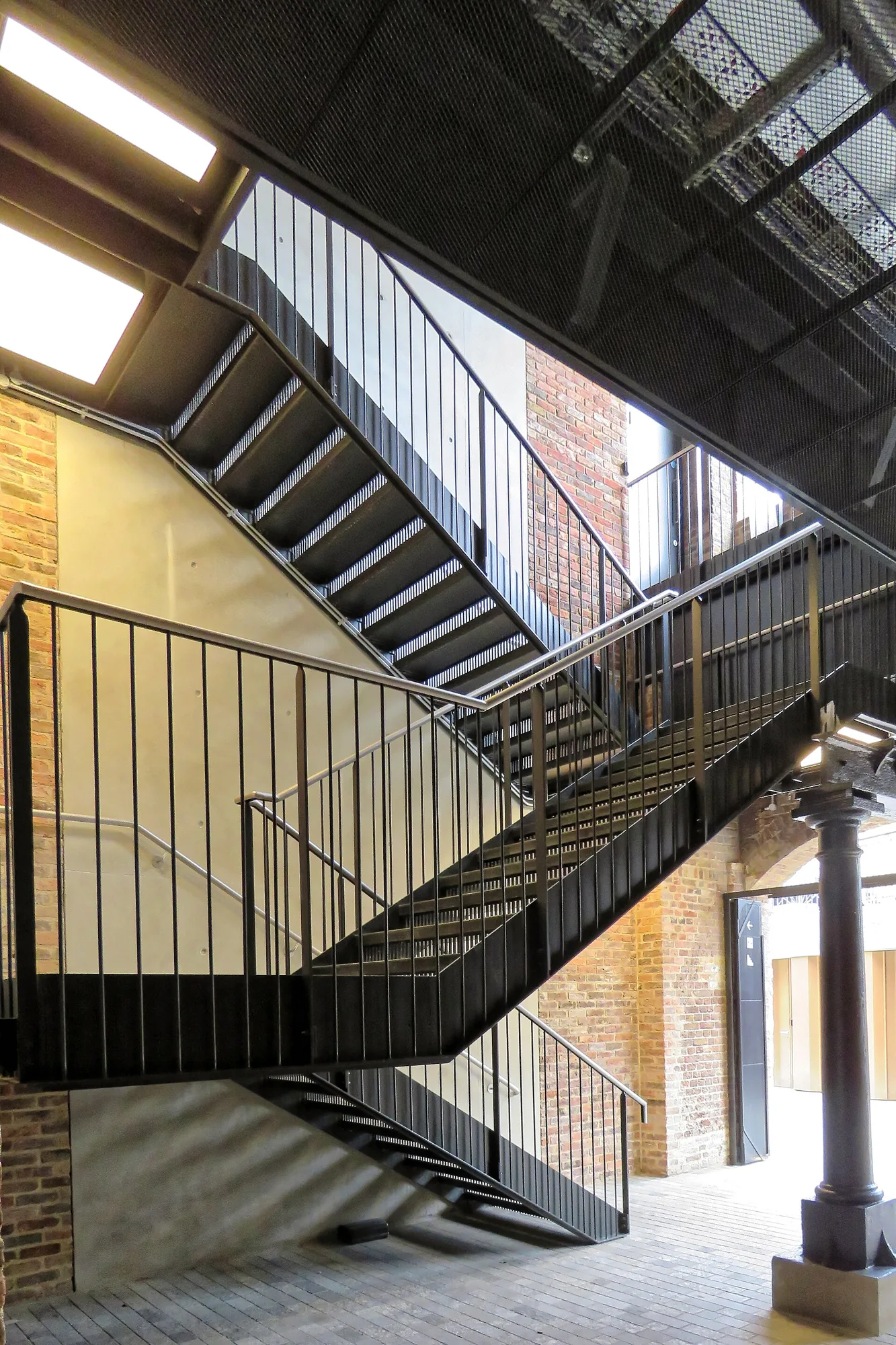 Zwarte stalen trap met verticale balustrades in een bakstenen doorgang